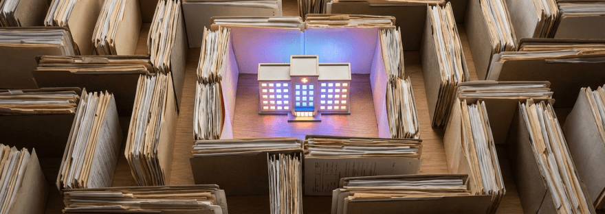 A small model building surrounded by a labyrinth of overflowing paper file folders.