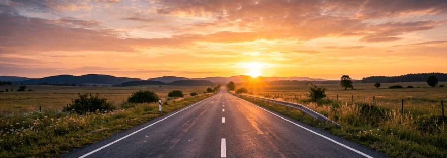 Empty rural road leading to sunset with fields and hills